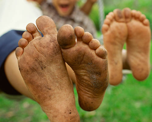A child show his bare feet covered in dirt.